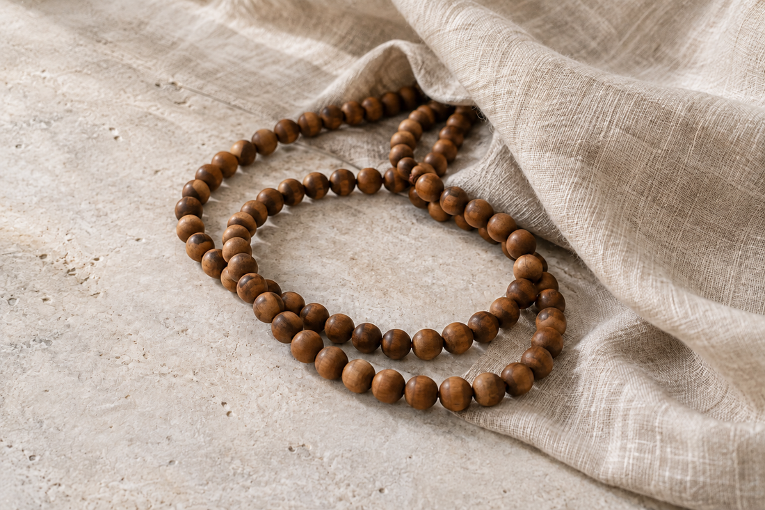 Brown wooden bead strand loosely coiled across pale stone and oatmeal linen.