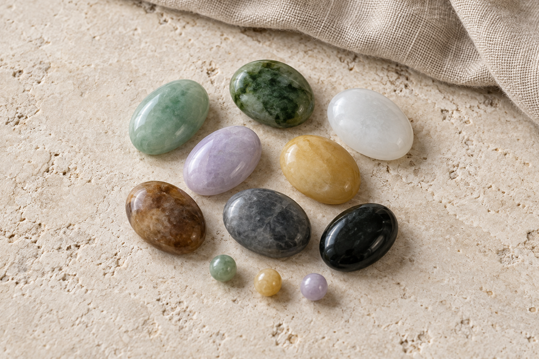 Polished green, white, lavender, yellow, brown, gray, and black oval pieces and beads arranged on pale stone.