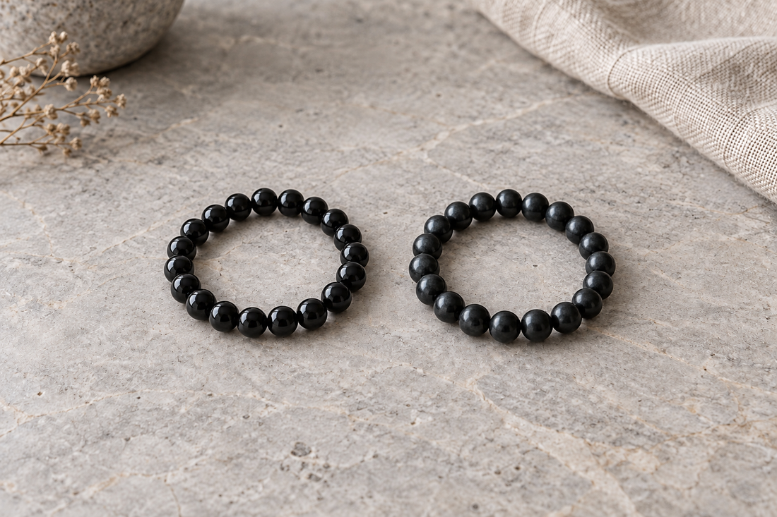 Two dark polished bead bracelets arranged side by side on a warm-gray stone surface.