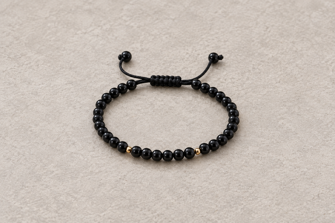 Black round-bead bracelet with dark cords and two gold-tone spacers on a warm gray surface.