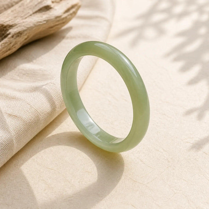 Smooth green jade bangle bracelet on textured fabric with natural light and leaf shadows
