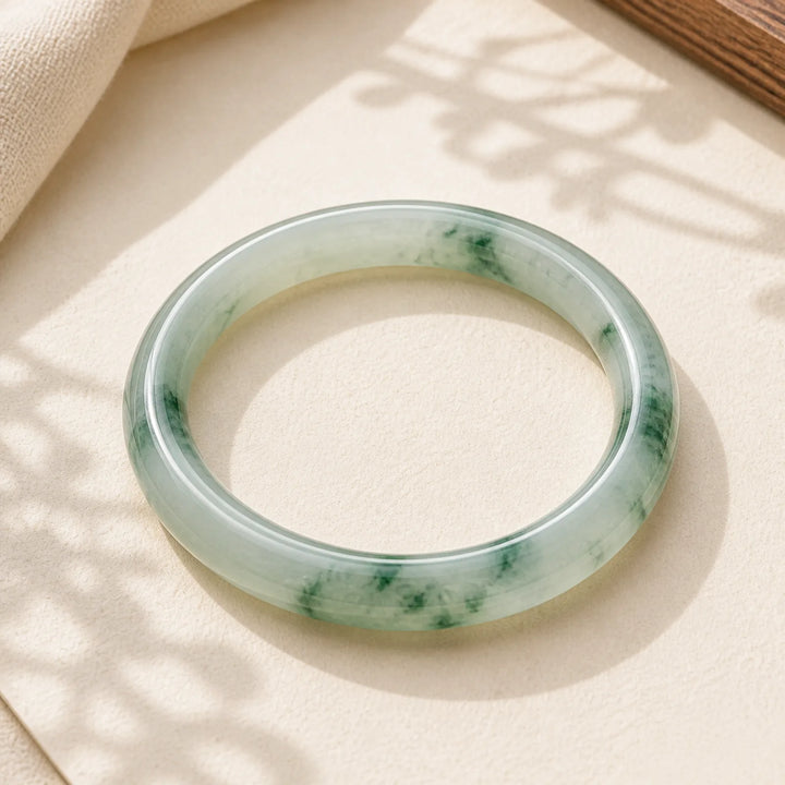 Handcrafted jade bangle with green inclusions, ideal for healing and protection