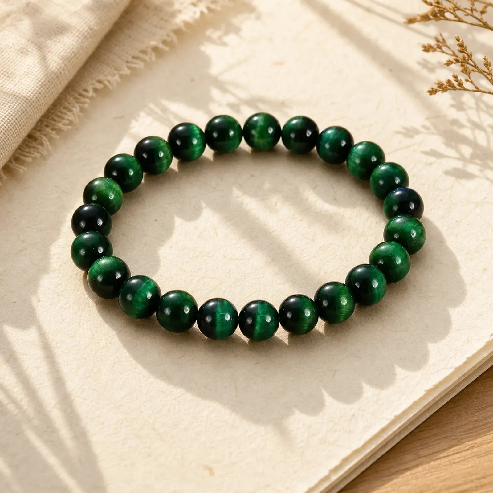 Green tiger eye gemstone bracelet on textured paper, natural light, dried flowers nearby
